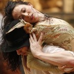 Dancer with black hair and in gold costume lifted on the back of another dancer with black hat