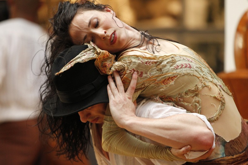 Dancer with black hair and in gold costume lifted on the back of another dancer with black hat