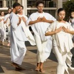 Dancers in white holding plates against their chests in prayer