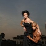 A woman walking on a ledge and held at the waist by a man