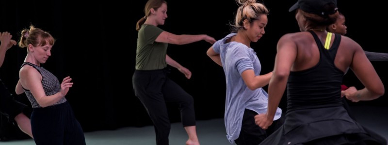 A few dancers try out movements as the teacher encourages them.