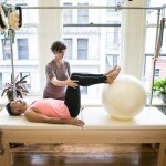 One body laying on a Pilates Cadillac with instructor assisting