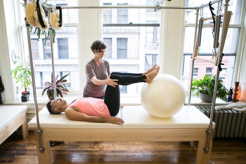 One body laying on a Pilates Cadillac with instructor assisting