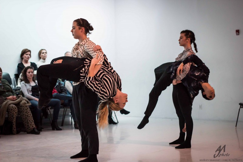 Four dancers are in front of an audience. Two dancers are being lifted and carried in two dancer's arms. 