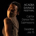 Female dancer in mask and tan shirt looks over her left shoulder in moody low light conditions