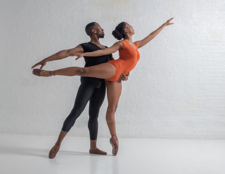 A pair of dancers stand in arabesque