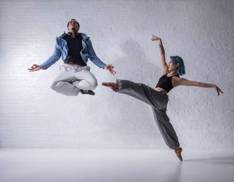 The image is of two dancers. One is jumping with legs crossed; the other is on pointe with leg and arms outstretched