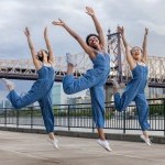 3 female dancers in blue jumpsuits, jumping in air arms overhead, Queensborough bridge in background