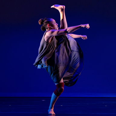 Dancer on blue lit stage photographed in a powerful high kick. 