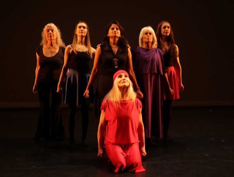 dancers standing and one sitting in red in front, defiant expression