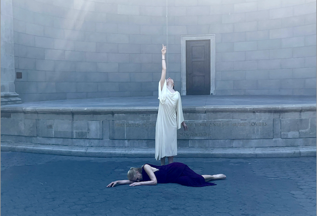 Dancer in Burgundy lying on ground, dancer in white standing in back of her, `arm raised and pointing to the sky