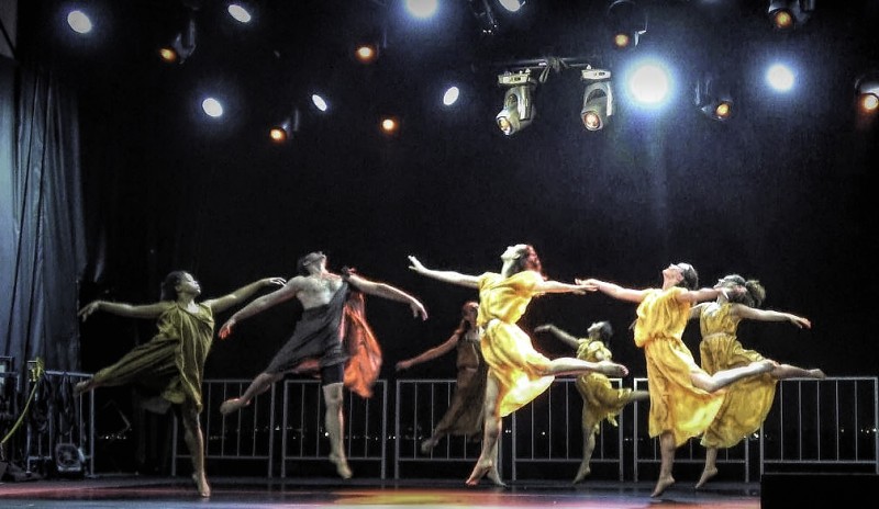 Several dancers in orange or brown tunics, in a  position of "abandon", leg in attitude back, arms extended, head thrown back