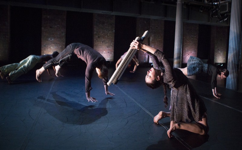 Two dancers, one holding a wooden board and leaning backwards, one in the air.