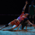   One dancer leans backward with one arm extended, supported by another dancer who crouches low and reaches forward