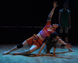   One dancer leans backward with one arm extended, supported by another dancer who crouches low and reaches forward