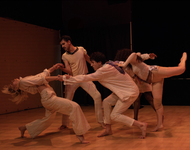Five dancers in neutral costumes perform an interconnected, dynamic movement sequence. 