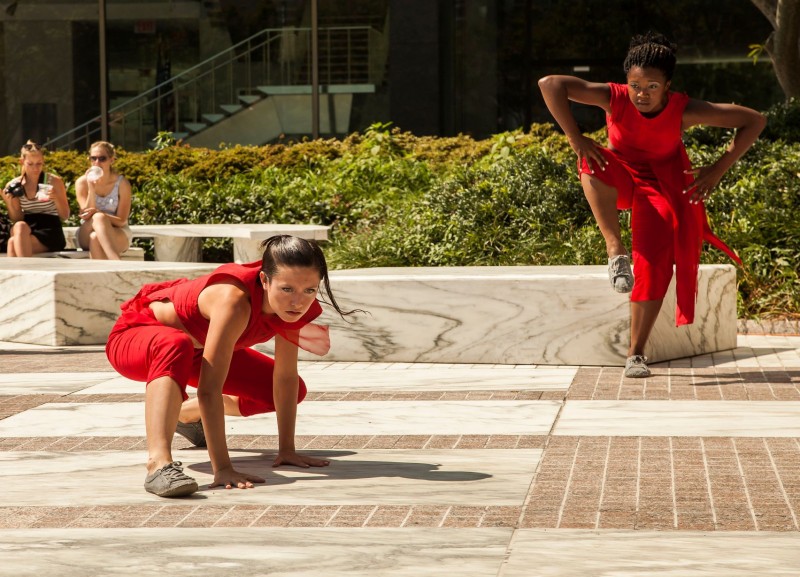Two dancers outfitted in red costumes perform on outdoor patio.