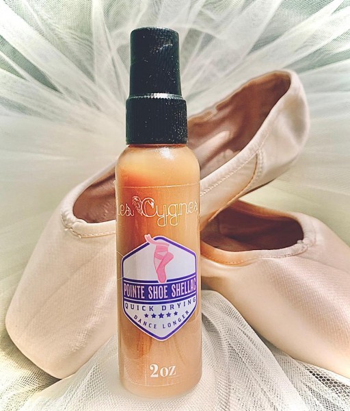 Bottle of pointe shoe shellac with pointe shoes against chiffon