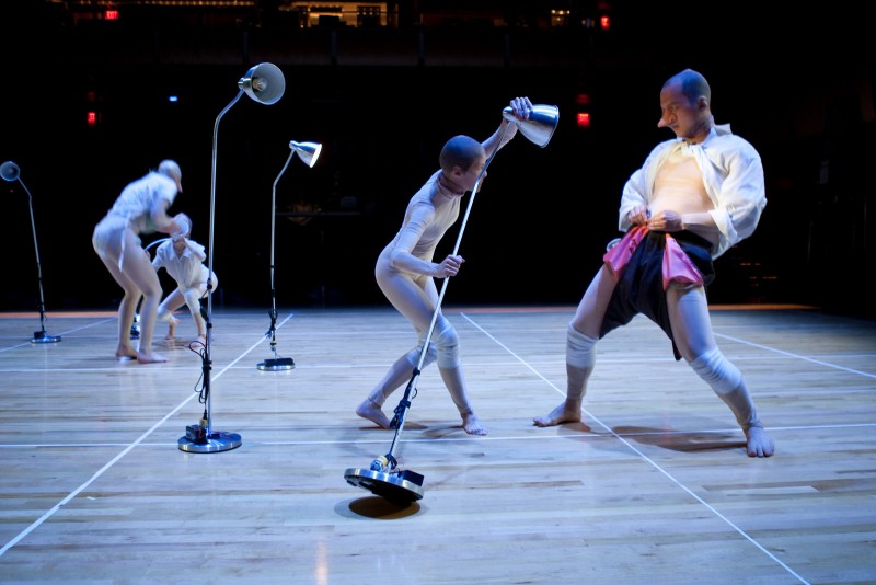 Dancer covered in mesh shines standing lamp on the torso of a dancer hinging backward.