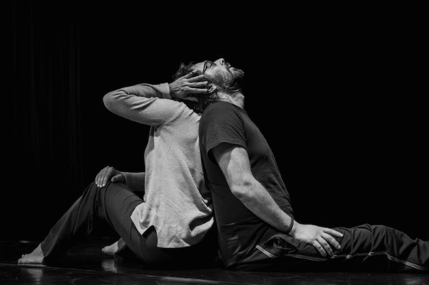 Two people sit back to back on the floor