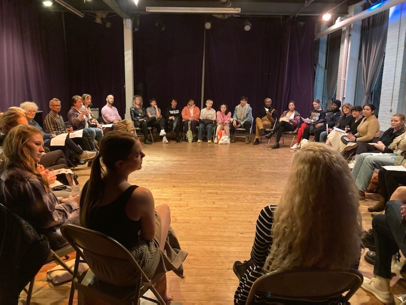 People are gathered in a circle sitting in chairs having a discussion 