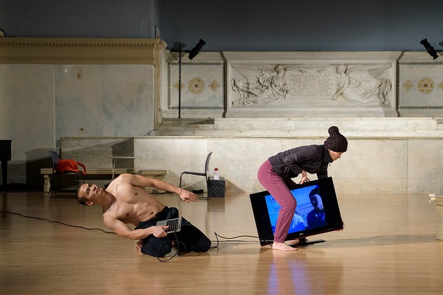 A man is sitting on the floor pulling on a TV cable. A woman, is pulling the opposite way with a TV in hand.