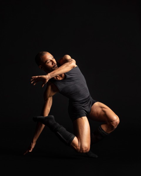 Dancer in black tank top, shorts, and leggings twisting right in a jump.