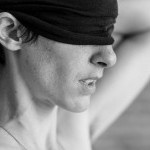 A black and white photo of a woman putting a blindfold on. 