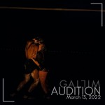 Two dancers embrace on a dark stage with white paint on their bodies.