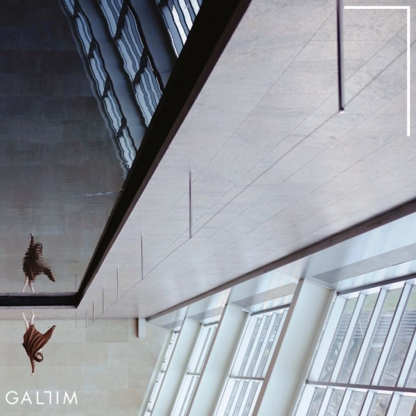 A dancer moves in a brown dress dances in front of a reflection pool inside of a large room with a marble floor and windows