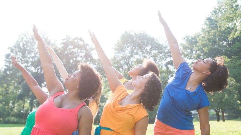 Five women dressed in different colors reach toward the sun.