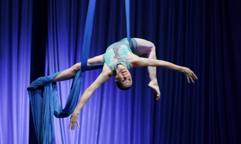 Female Aerial dancer in blue leotard hanging upside down suspended by silks