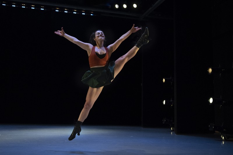 A woman in a jump kick with her leg out to the side and her arms extended upward
