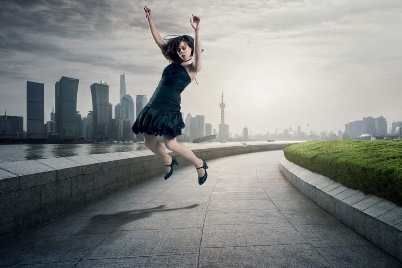 Dancer in black cocktail dress and heels jumping with hips forward, arms overhead, and legs back