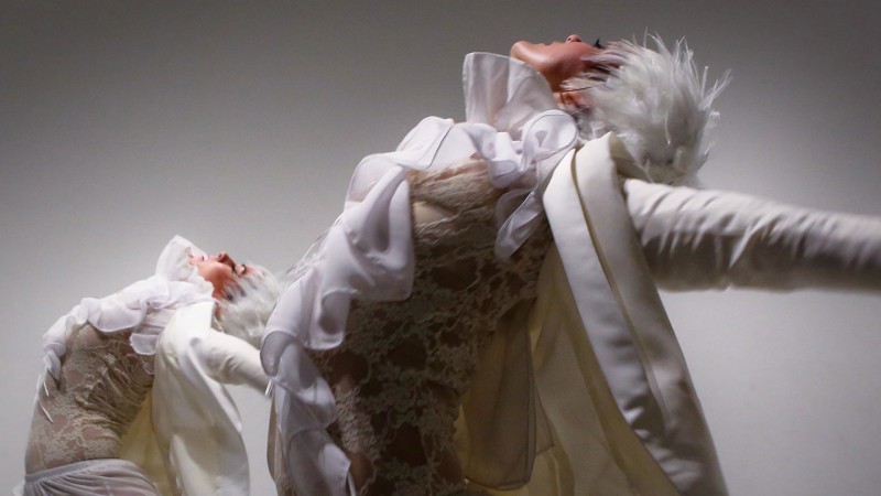 Two dancers dancing and wearing white ruffled shirts and wigs 
