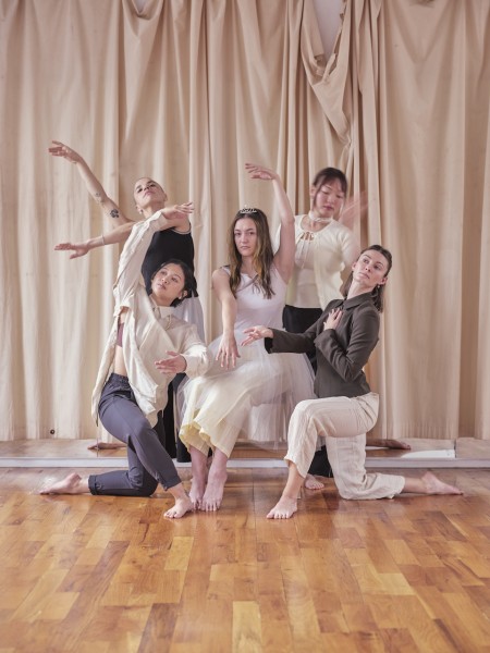 Photo of Julia sitting on a stool surrounded by 4 dancers in ballet poses.