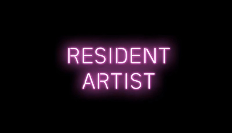 Image of a pink neon sign against a black background that reads 'Resident Artist'