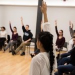 Group of people sitting in a circle with one arm raised in the air.