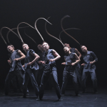 Group of dancers with feathers breezing over their heads.
