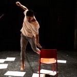 Two men jumping between chairs with paper on the floor.