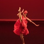Female Dancer in Red Dress Kicking Leg to Front with opposite arm extending upward