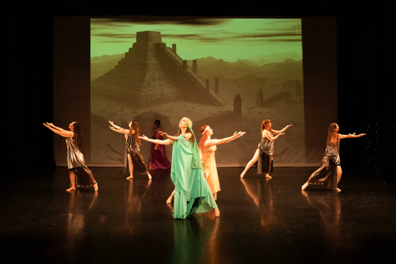 Dancers in costuming representing Ancient Mesopotamia, pose in front of a backdrop of a ziggurat.