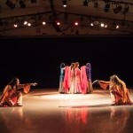 Two dancers in foreground reach toward each other; two dancers in background drape red veils over two women between them.