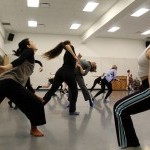 Multiple dancers in workout clothing and socks moving as a group