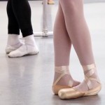 Two dancers, one male and one female, stand at the barre in 5th position.