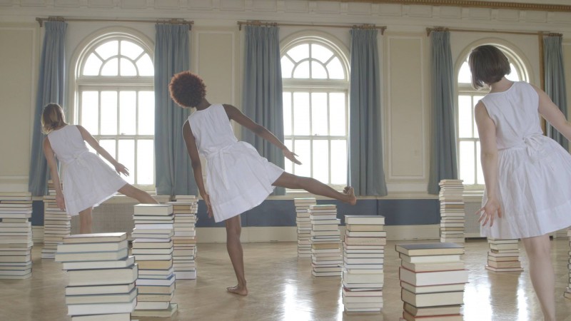 Three women standing on one leg in a room full of books.