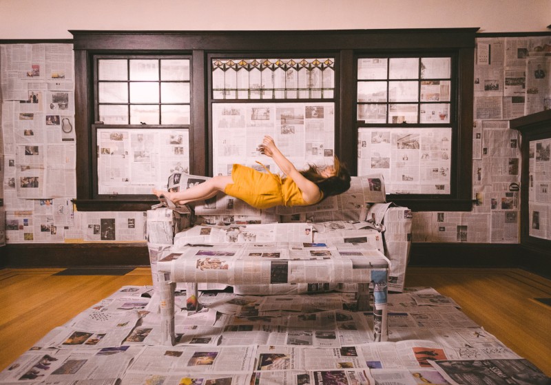 woman in yellow dress falls onto couch covered in newspaper