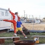 A man in a bright orange suit jumps as a man in a blue shirt and bright yellow shorts watches.