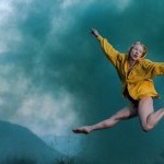 Woman in a yellow shirt jumping in a cloud of green smoke.