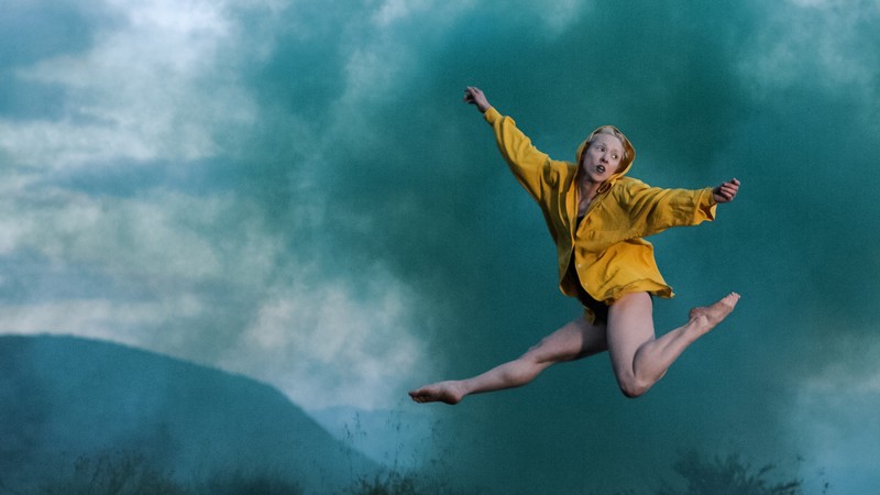 Woman in a yellow shirt jumping in a cloud of green smoke.